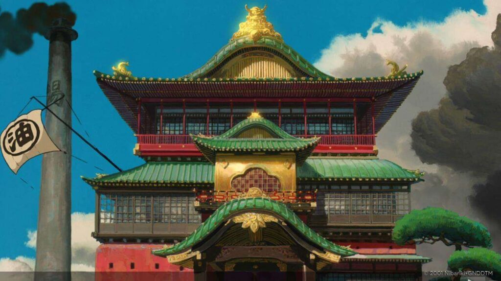 An ornate bath house with green sloped roofs and gold detailing from the movie Spirited Away.