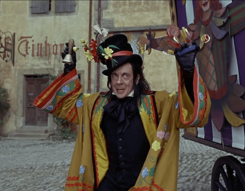 The Child Catcher from Chitty Chitty Bang Bang - a man with a large nose, black hair, and a floral yellow robe holding candy and a bell in the other hand. 